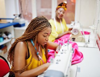 Two african dressmaker woman sews clothes on sewing machine at tailor office. Black seamstress girls.