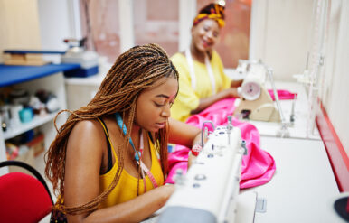Two african dressmaker woman sews clothes on sewing machine at t Two african dressmaker woman sews clothes on sewing machine at tailor office. Black seamstress girls.